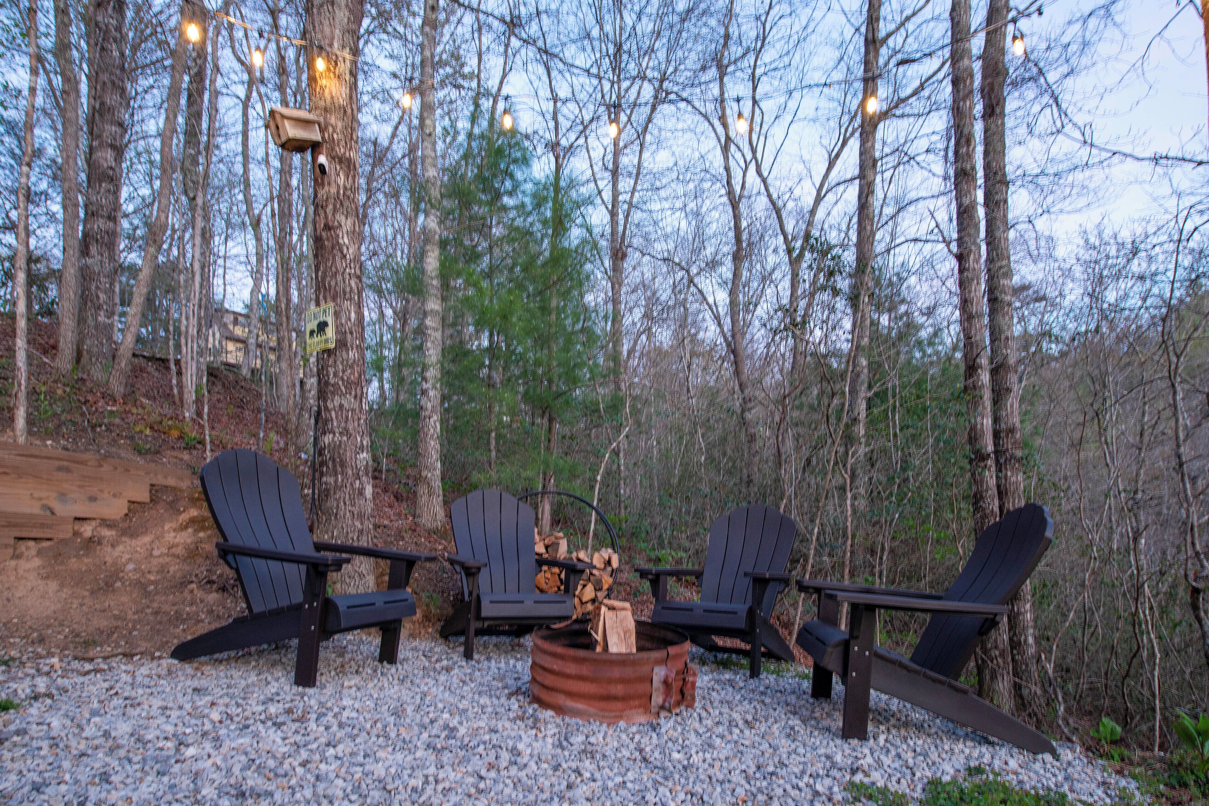 Un décor forestier avec des fauteuils Adirondack disposés autour d’un foyer, le tout entouré d’arbres et agrémenté d’une terrasse en bois.