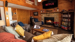 A cozy living room with a fireplace, a bookshelf, and a TV mounted on the wall. - Hot Tub Private Mtn-view Deck Family Cabin (Almond)