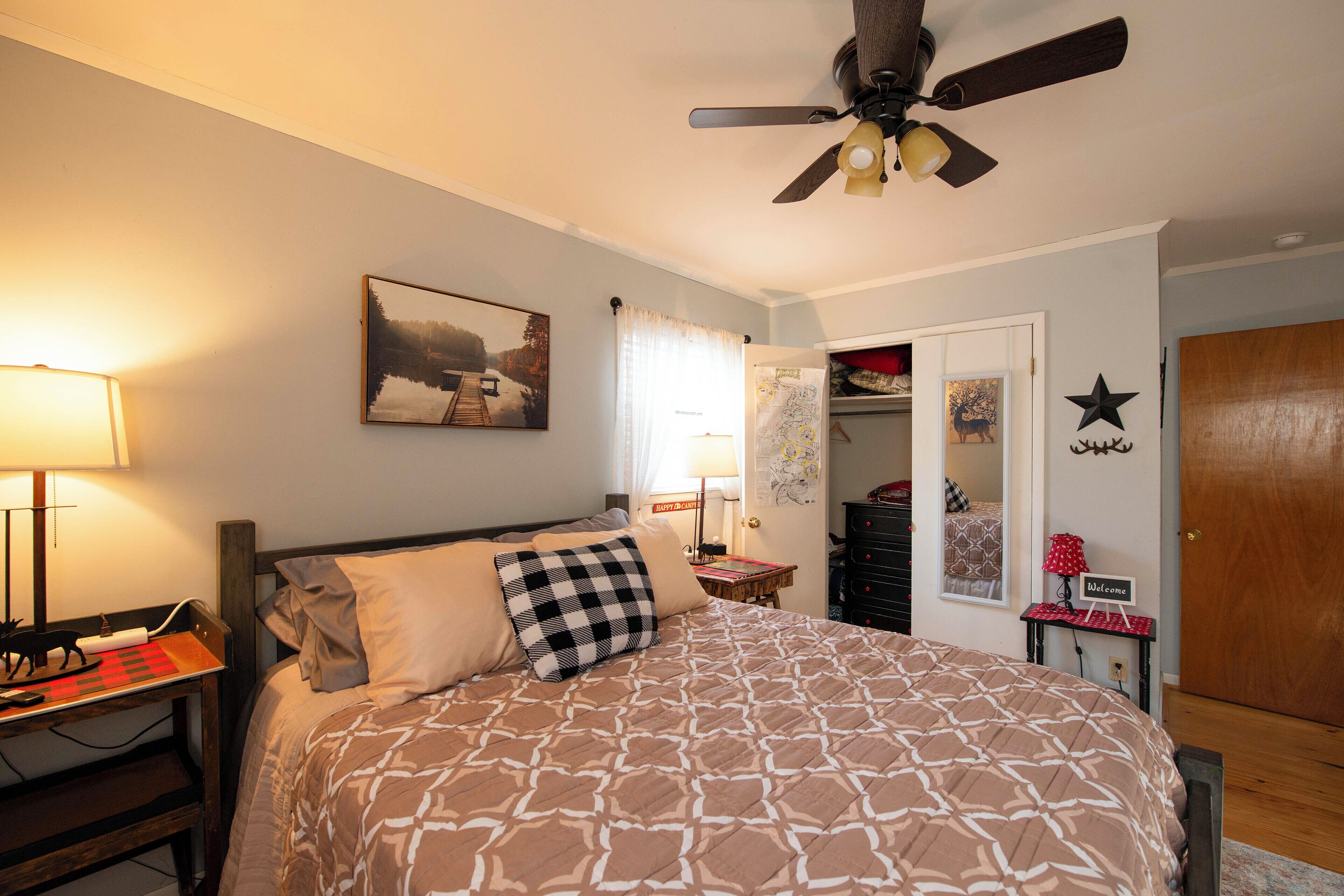 A bedroom with a bed, a desk with a lamp, a ceiling fan, a door, and a closet.