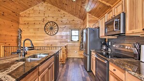 L’intérieur d’un chalet en bois comprend une cuisine dotée de plans de travail en granit, d’appareils électroménagers en acier inoxydable et d’une grande fenêtre.