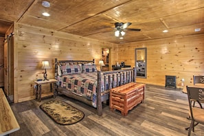 A cozy log cabin bedroom with a wooden bed, a nightstand, a bench, a mirror, and a small heater. - Smoky Mtn Log Cabin w/ Hot Tub & Panoramic Views! (Sevierville)
