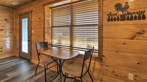 Un intérieur en bois avec une table et des chaises, une fenêtre avec des stores et une enseigne murale sur laquelle on peut lire « Bonjour ».