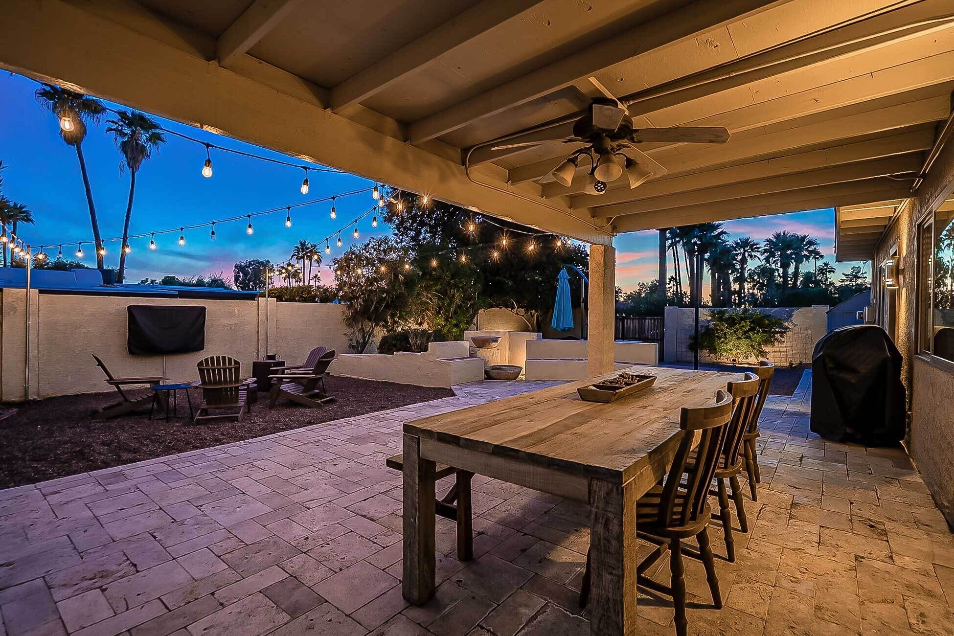 An outdoor patio with a wooden table and chairs, string lights, and a ceiling fan.