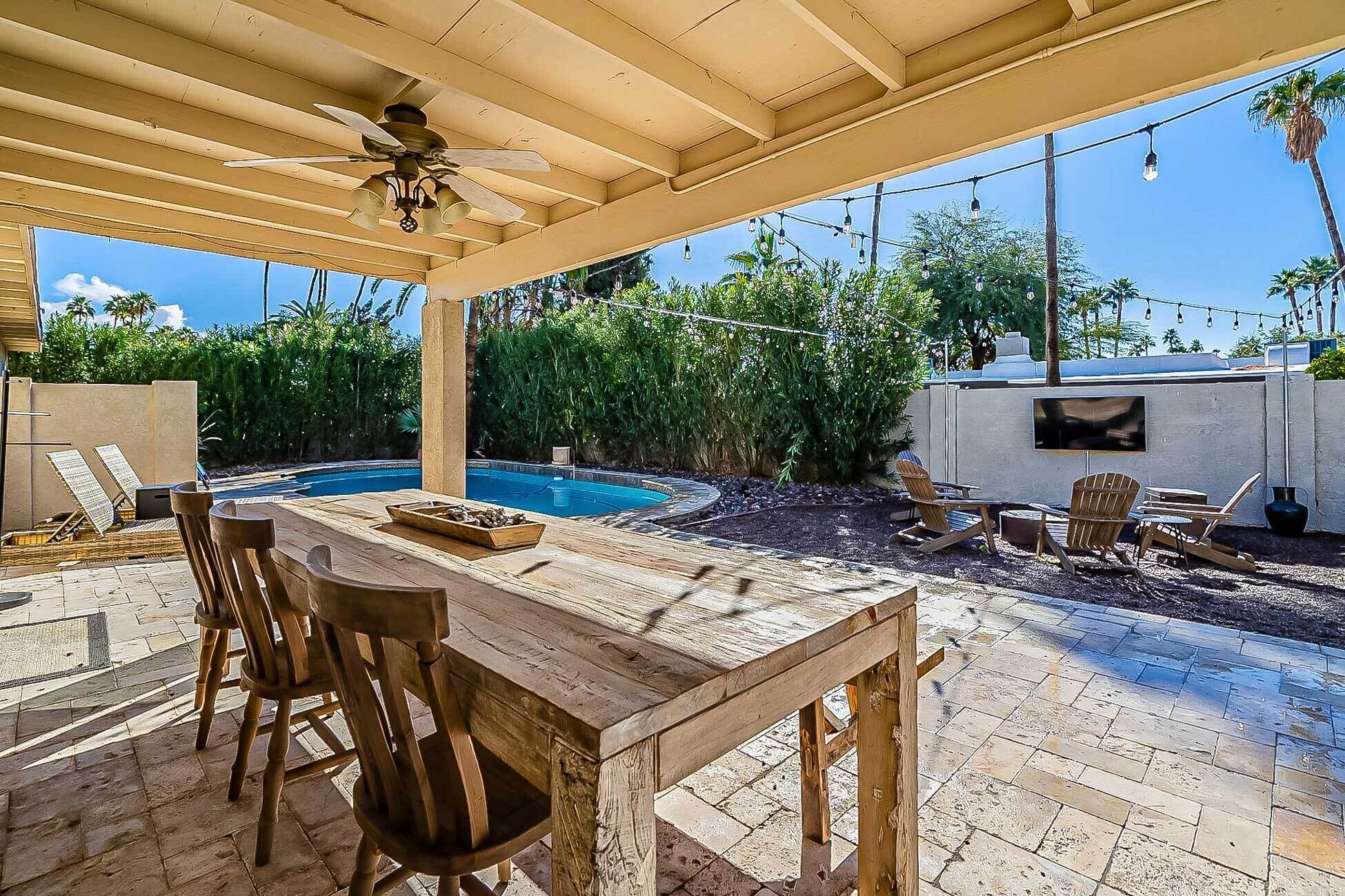 Eine überdachte Terrasse im Freien mit Pool, Holzmöbeln und Deckenventilator.
