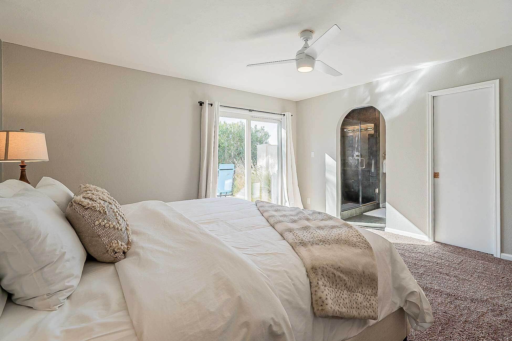 A bedroom with a bed, a ceiling fan, a window, and a door leading to a bathroom.