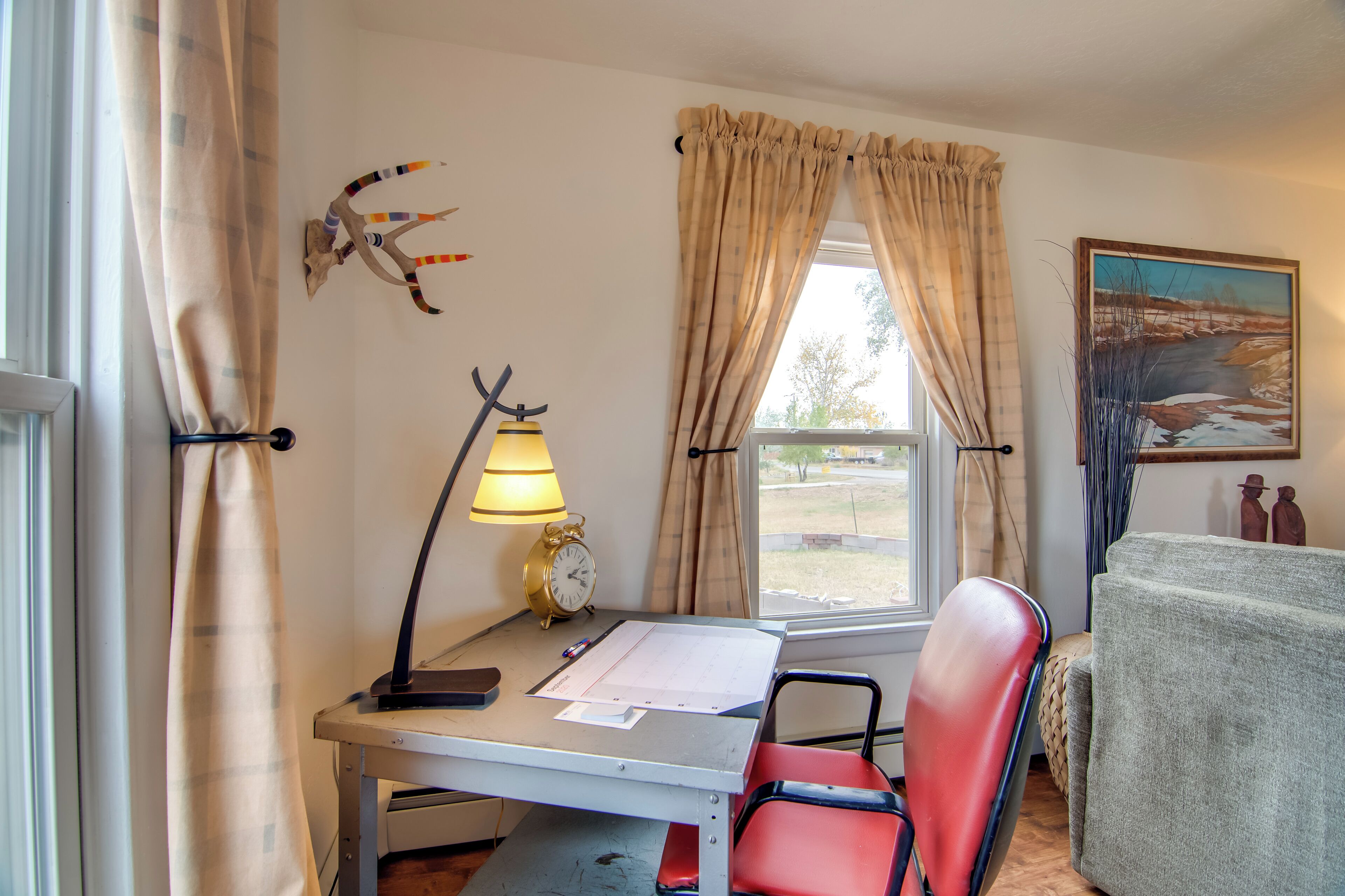 A room with a desk, chair, lamp, clock, and a painting.