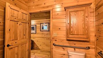 A wooden-paneled bathroom with a toilet, a handrail, and framed pictures on the wall.