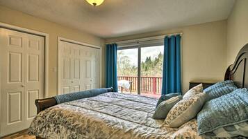 A bedroom with a bed, a window with curtains, a ceiling light, and a view of a balcony.