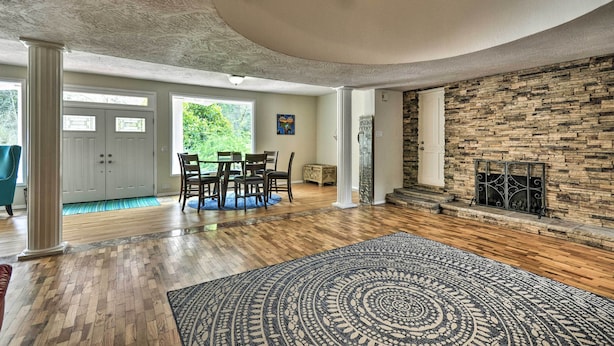 A spacious living room with hardwood flooring, a large rug, a stone fireplace, and a dining area with chairs and a table. - Charming Kelso Home w/ Proximity to Cowlitz River! (Kelso)