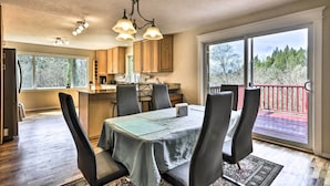 A dining area with a table set for four, a kitchen in the background, and a balcony with a red railing. - Charming Kelso Home w/ Proximity to Cowlitz River! (Kelso)