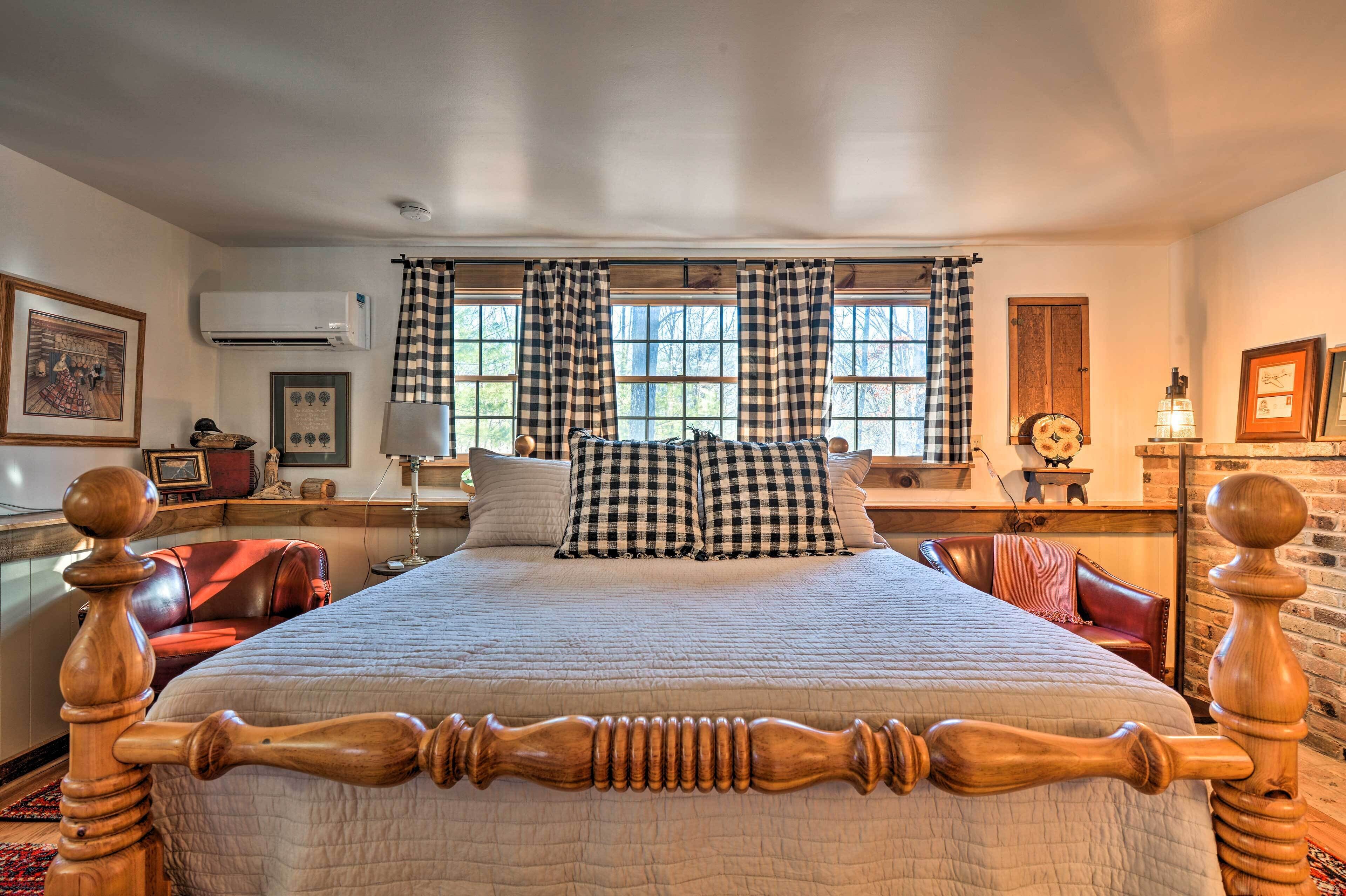 A bedroom with a large bed, checkered curtains, a wooden headboard, and a window with a view of trees.