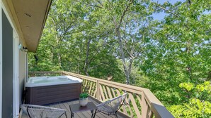 A wooden deck with a hot tub, two wicker chairs, and a small table with a plant.
