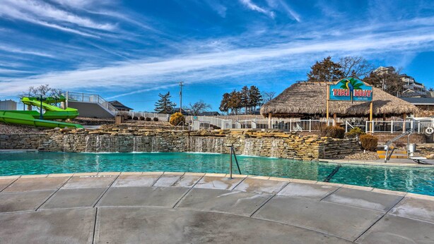 A swimming pool area with a sign for 'TIKI HUT', a thatched-roof structure, and a waterfall feature.