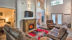 A modern living room with leather sofas, a fireplace, a flat-screen TV, and a large window. - Home w/ Hot Tub < 5 Miles to Rainier National Park (Mineral)