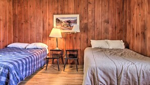 A room with wooden panel walls, two beds with different bedding, a desk with a lamp, and a framed picture on the wall. - Dent Cabin on Star Lake w/ Dock, Deck, Dining (Dent)