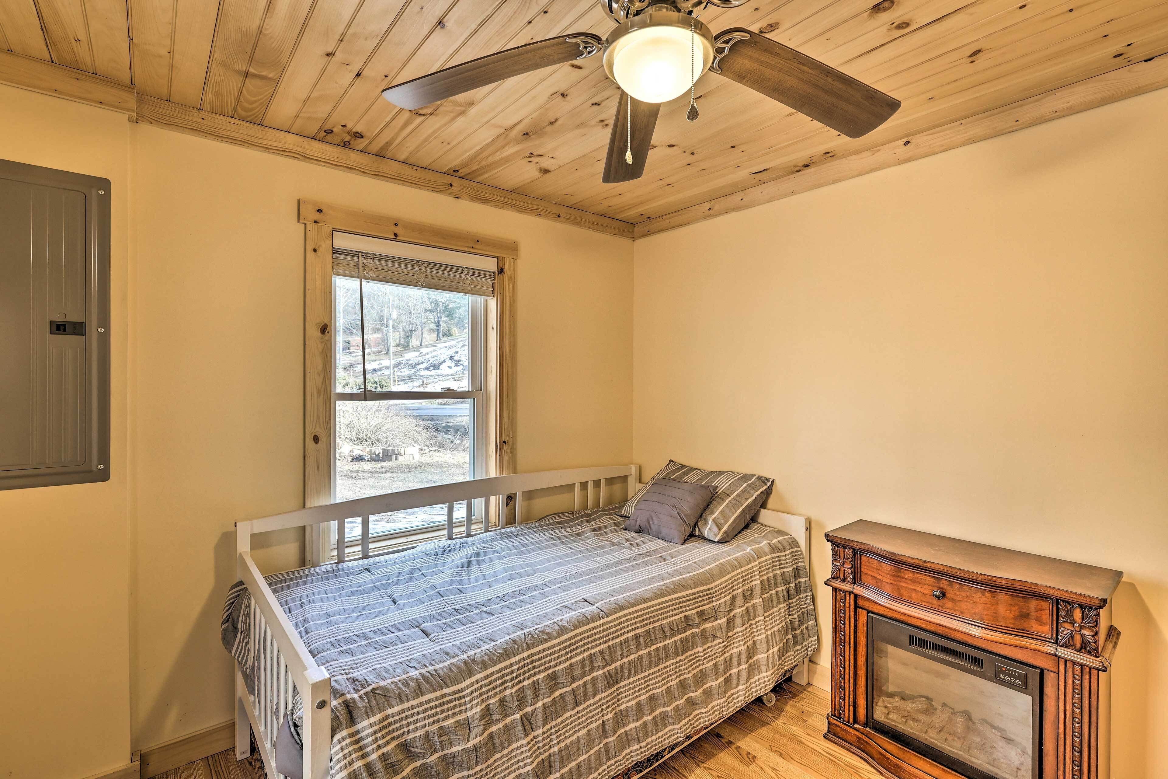 A bedroom with a single bed, a wooden ceiling fan, a window, and a wooden cabinet.