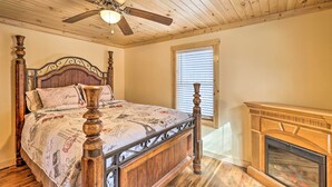 Un dormitorio con techo de madera, una cama con cabecera decorativa, un ventilador de techo y una chimenea.
