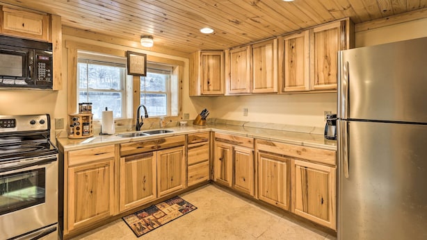 A kitchen with wooden cabinets, stainless steel appliances, and a window with a view of trees. - Quaint Appalachian Getaway ~ 2 Mi to Boone! (Boone)