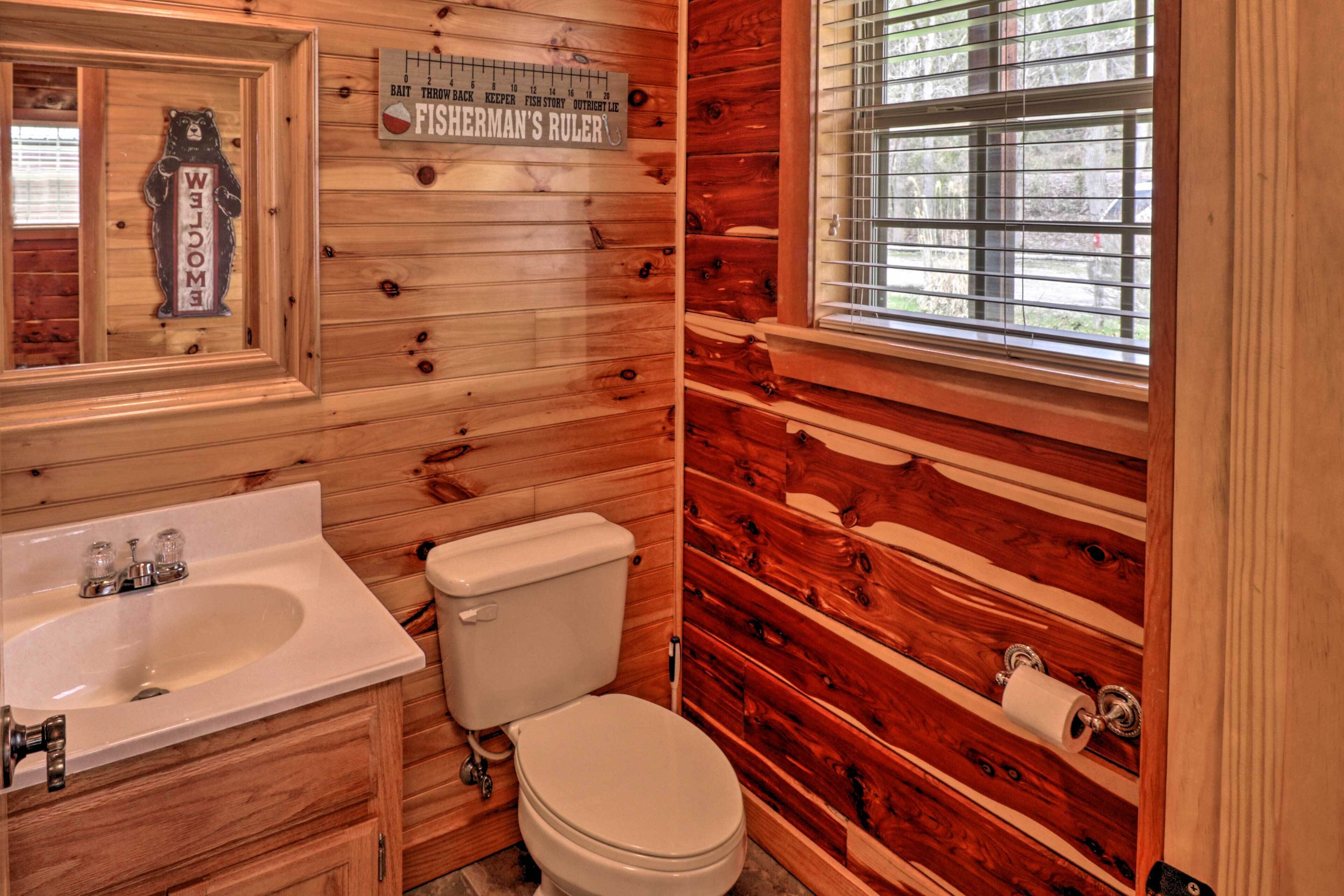 Ein Badezimmer in einer Holzhütte mit Waschbecken, Toilette und einem Fenster mit Jalousien.