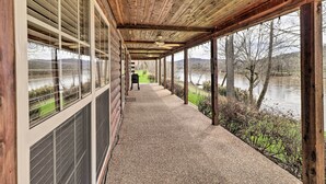 Überdachte Veranda mit Blick auf einen Fluss und Bäume, Holzboden und Kiesboden.