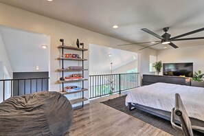 A modern bedroom with a large bed, a ceiling fan, a TV, and a bookshelf with board games. - Fire Pit, Deck & Mtn Views: Upscale Pine Cabin! (Pine)