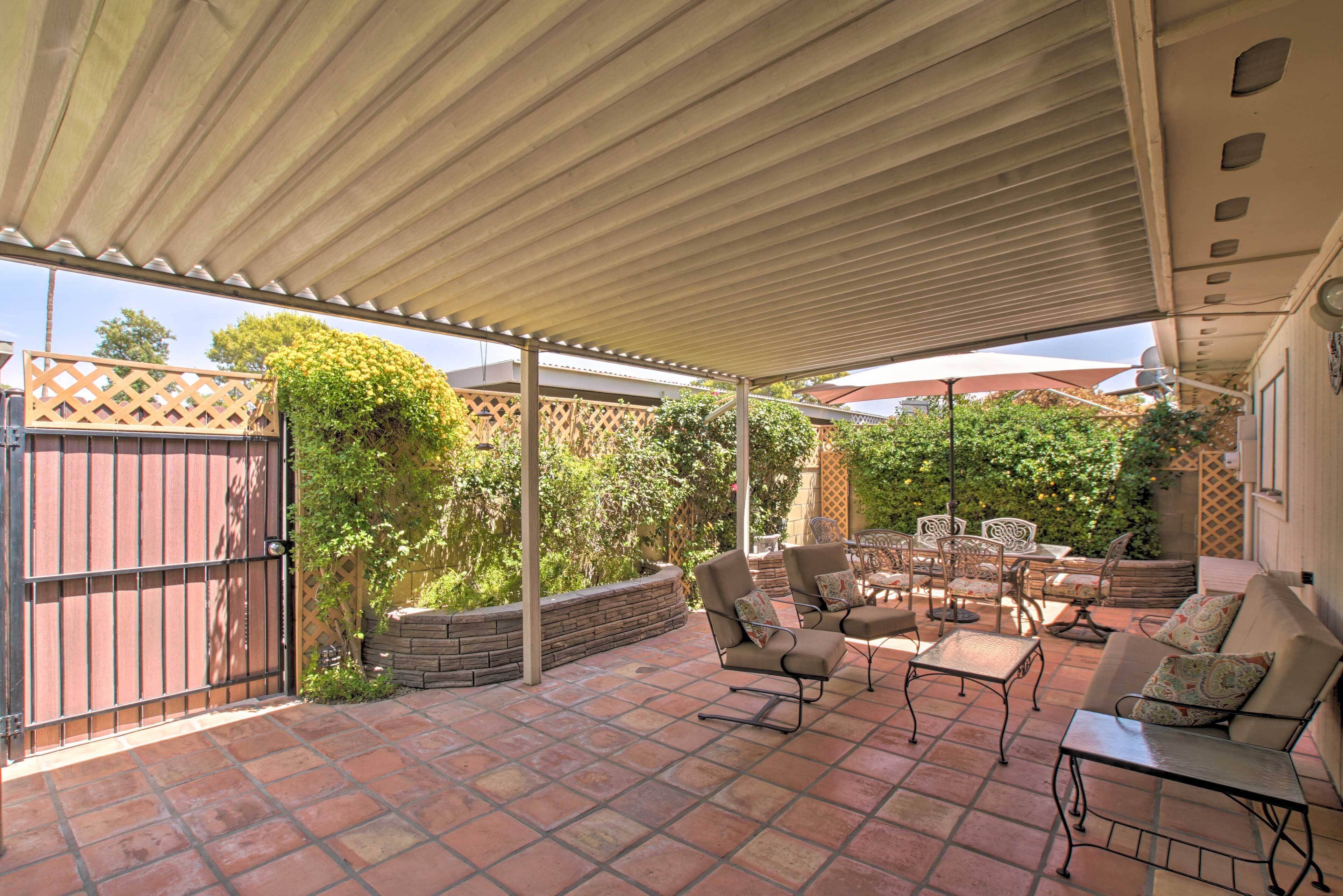 Un patio al aire libre con zona cubierta, suelo de piedra y mobiliario exterior.
