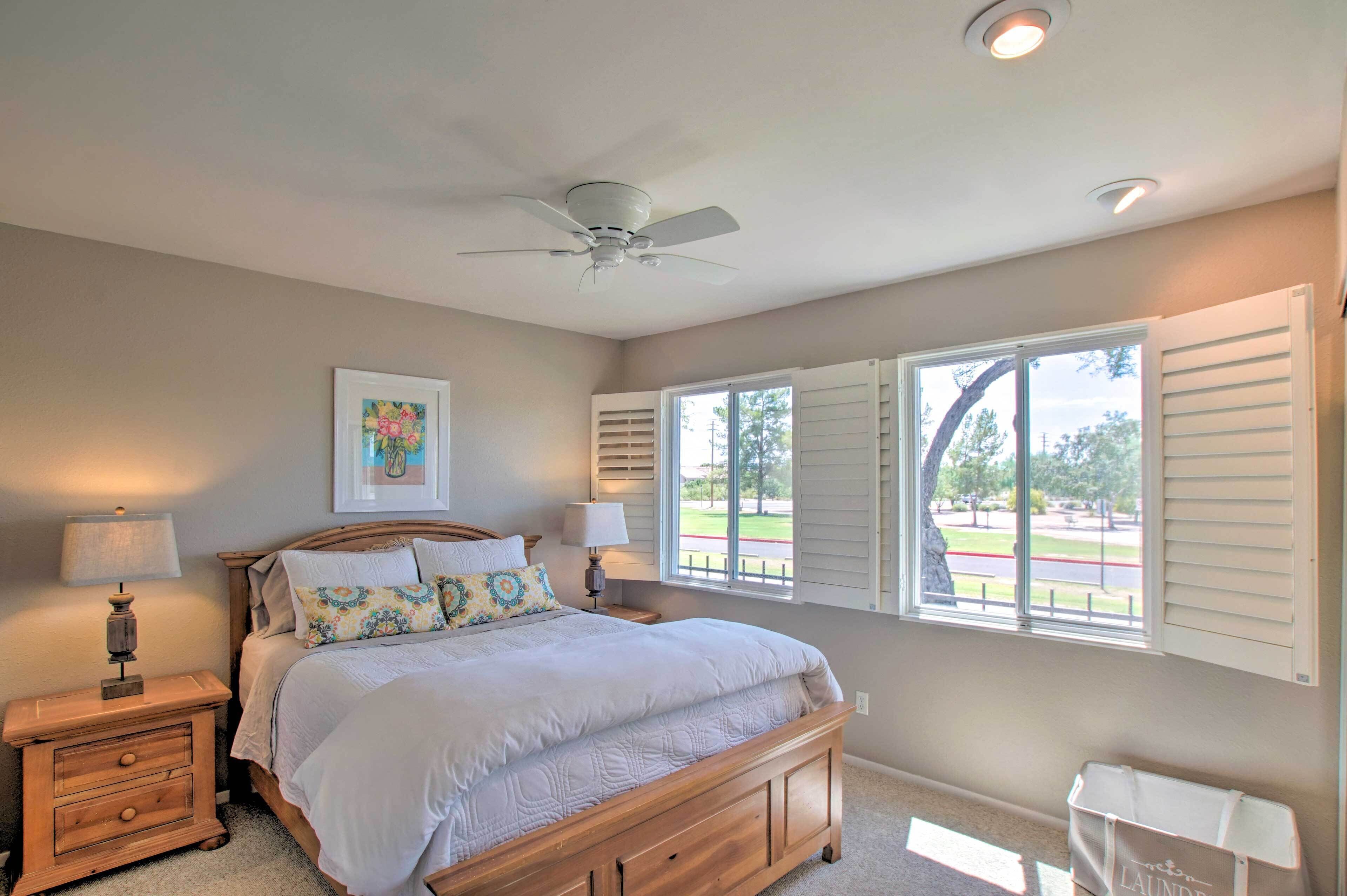 A bedroom with a bed, bedside lamps, a ceiling fan, and a window with shutters.