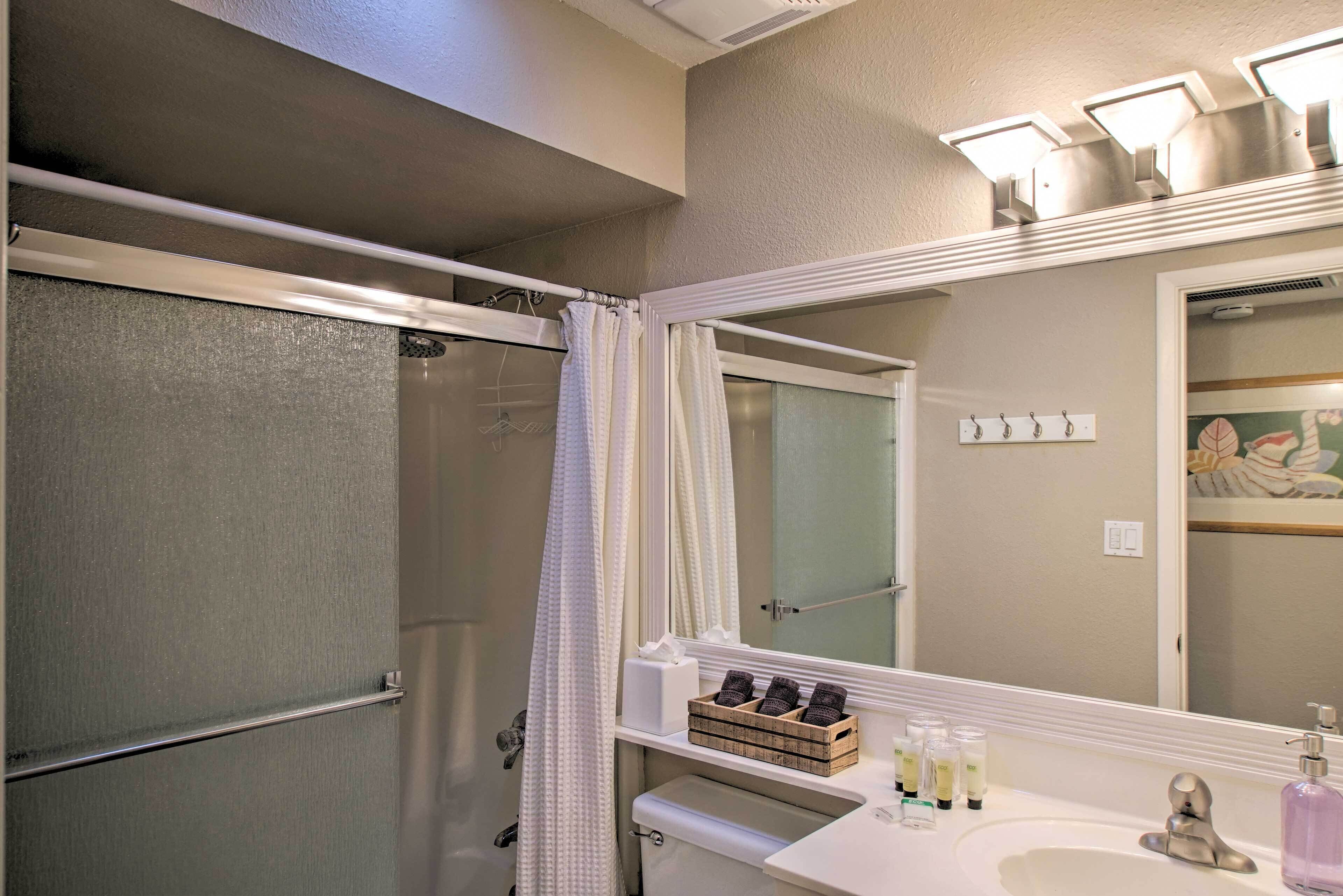 A bathroom with a shower, a sink with toiletries, and a mirror.