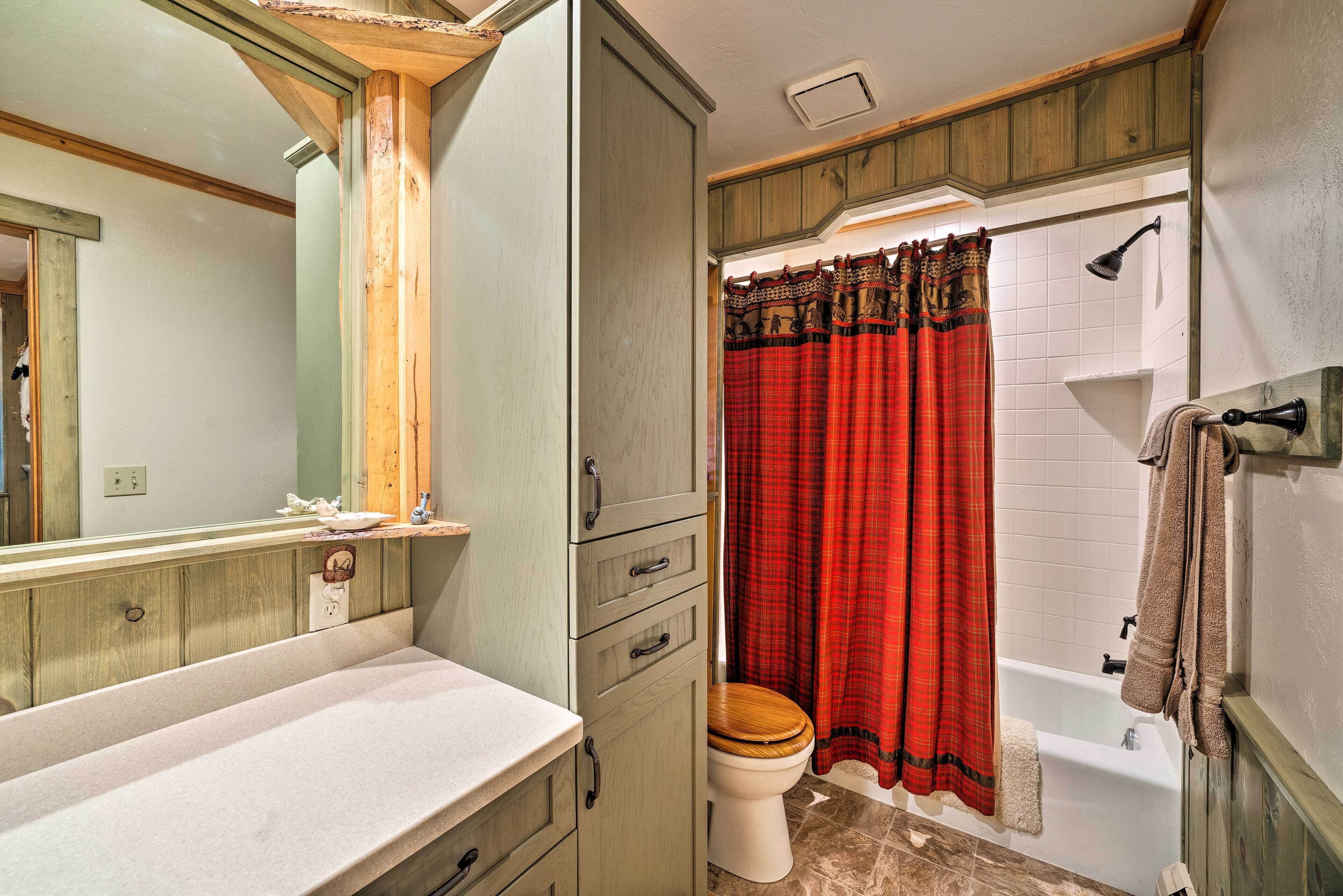 A bathroom with a wooden vanity, a toilet, a shower with a red curtain, and a mirror.