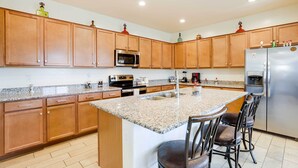 Una cocina moderna con armarios de madera, encimeras de granito, un refrigerador de acero inoxidable y una isla central con taburetes de bar.