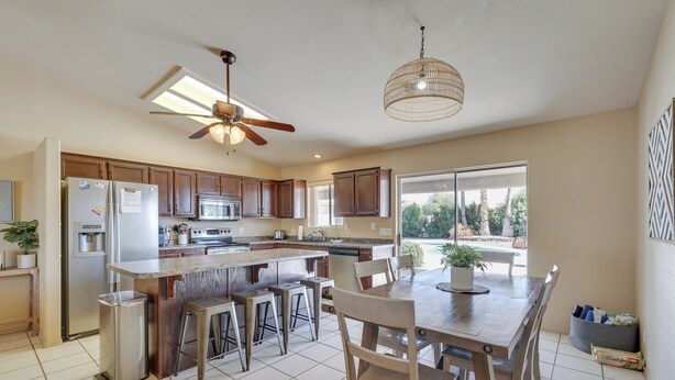 A modern kitchen with wooden cabinets, a central island, and a dining area with chairs. - Lake Havasu Getaway w/ Pool, Hot Tub & Game Room (Lake Havasu City)