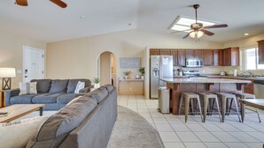 A modern kitchen with wooden cabinets, a central island with stools, and a ceiling fan. - Lake Havasu Getaway w/ Pool, Hot Tub & Game Room (Lake Havasu City)