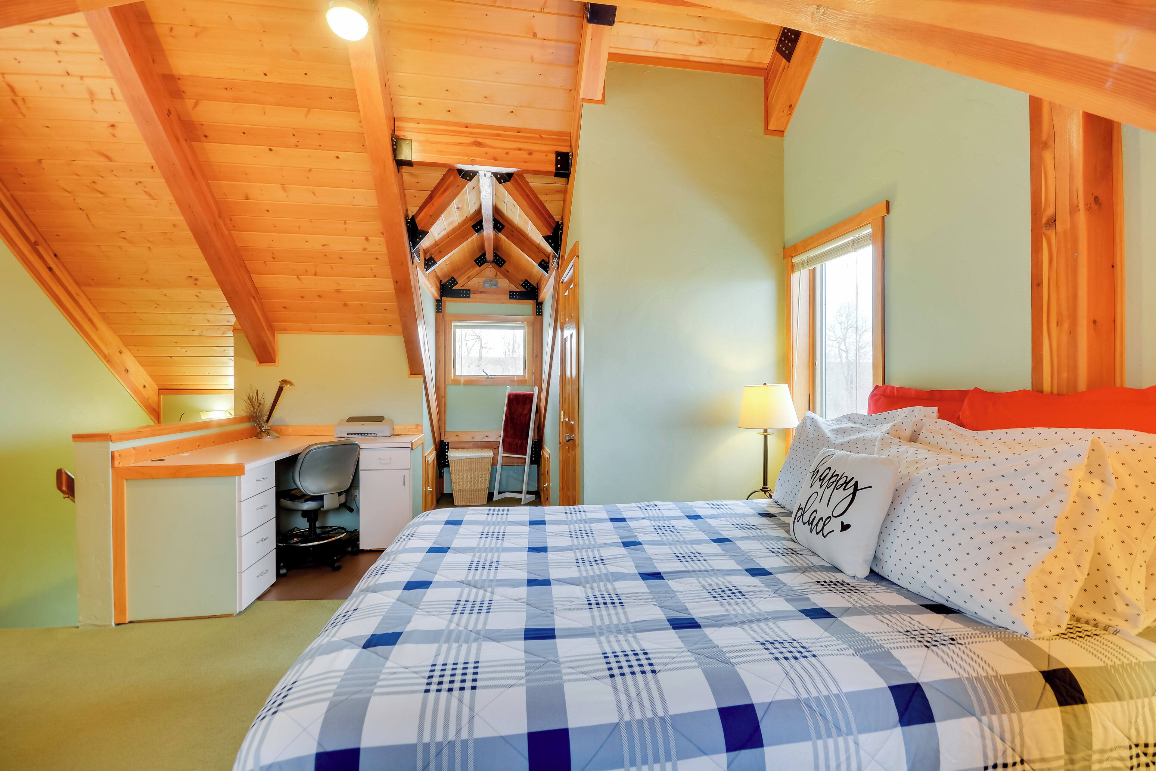 Un dormitorio con cama, escritorio y silla, una ventana y una puerta que da a otra habitación.