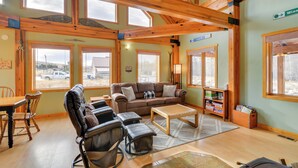 A spacious room with a large window, a brown sofa, a wooden coffee table, and a massage chair. - 'off The Beaten Path' Cabin w/ Mtn Views & Hot Tub (Red Lodge)