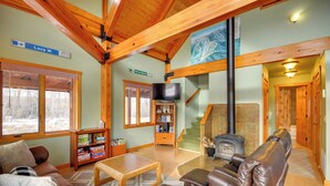 A spacious living room with a fireplace, a television, and a bookshelf. - 'off The Beaten Path' Cabin w/ Mtn Views & Hot Tub (Red Lodge)