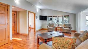 A spacious living room with hardwood floors, a large flat-screen TV mounted on the wall, and two patterned armchairs.