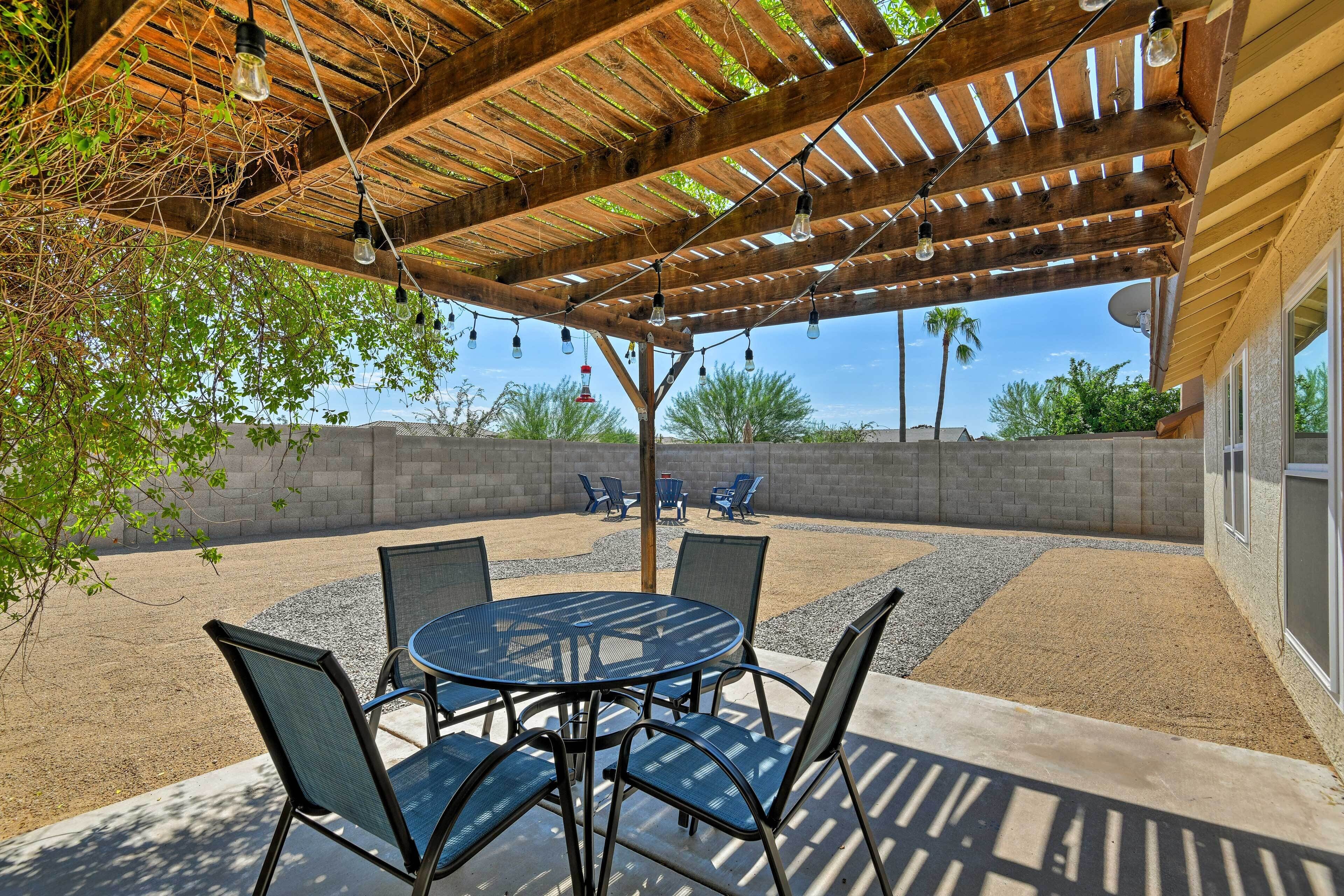 An outdoor patio with a round table and chairs, a pergola with hanging lights, and a view of the surrounding landscape.