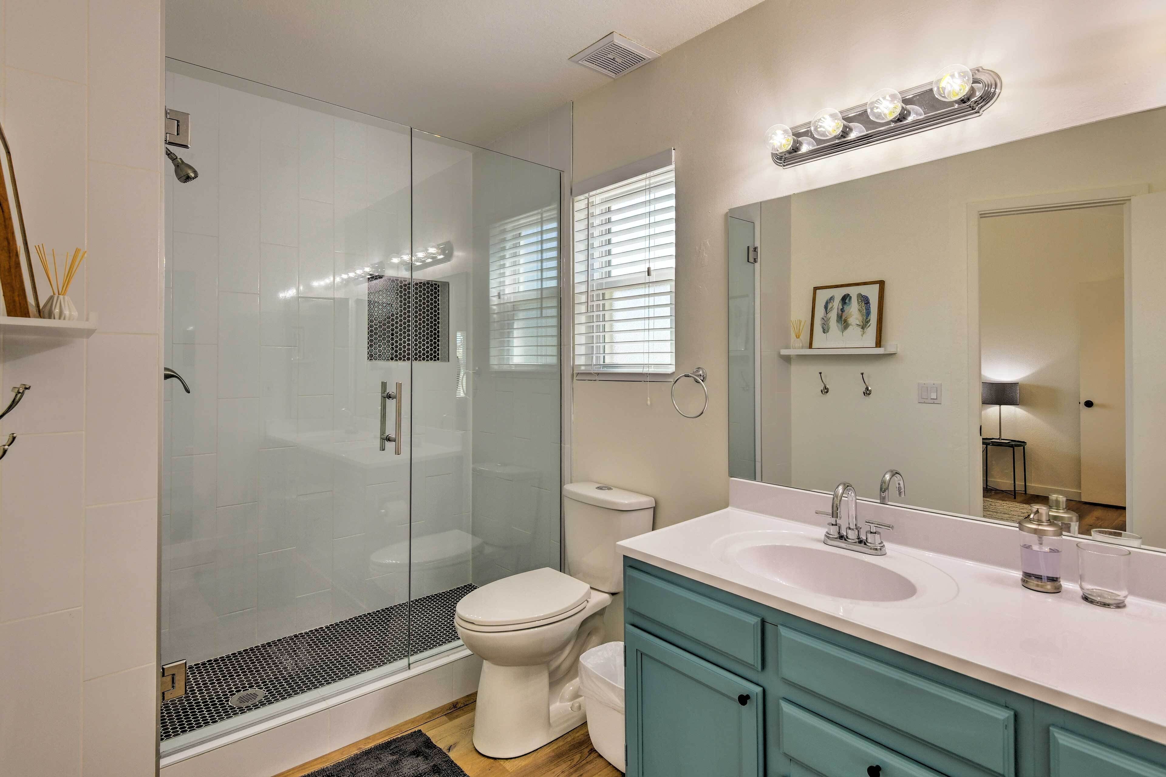 A modern bathroom with a glass-enclosed shower, a white toilet, and teal cabinets.