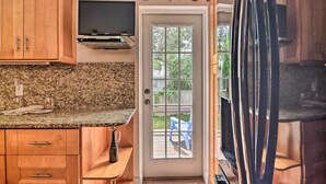 A kitchen with wooden cabinets, granite countertops, a built-in TV, and a door leading to a patio with a blue chair. - Seminole Home: 1 Mi to Indian Shores Beach! (Seminole)