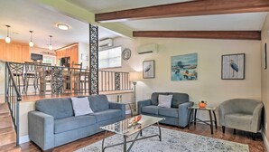 A spacious living area with a gray sofa, a coffee table, and a gray armchair. A staircase with a railing leads to a kitchen area in the background. - Seminole Home: 1 Mi to Indian Shores Beach! (Seminole)
