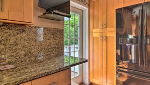 A kitchen with granite countertops, wooden cabinets, a stainless steel refrigerator, and a window with a view of greenery. - Seminole Home: 1 Mi to Indian Shores Beach! (Seminole)
