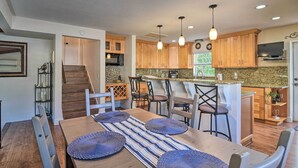 A modern kitchen with wooden cabinets, a central island, pendant lighting, and a dining area with a striped table runner and woven placemats. - Seminole Home: 1 Mi to Indian Shores Beach! (Seminole)
