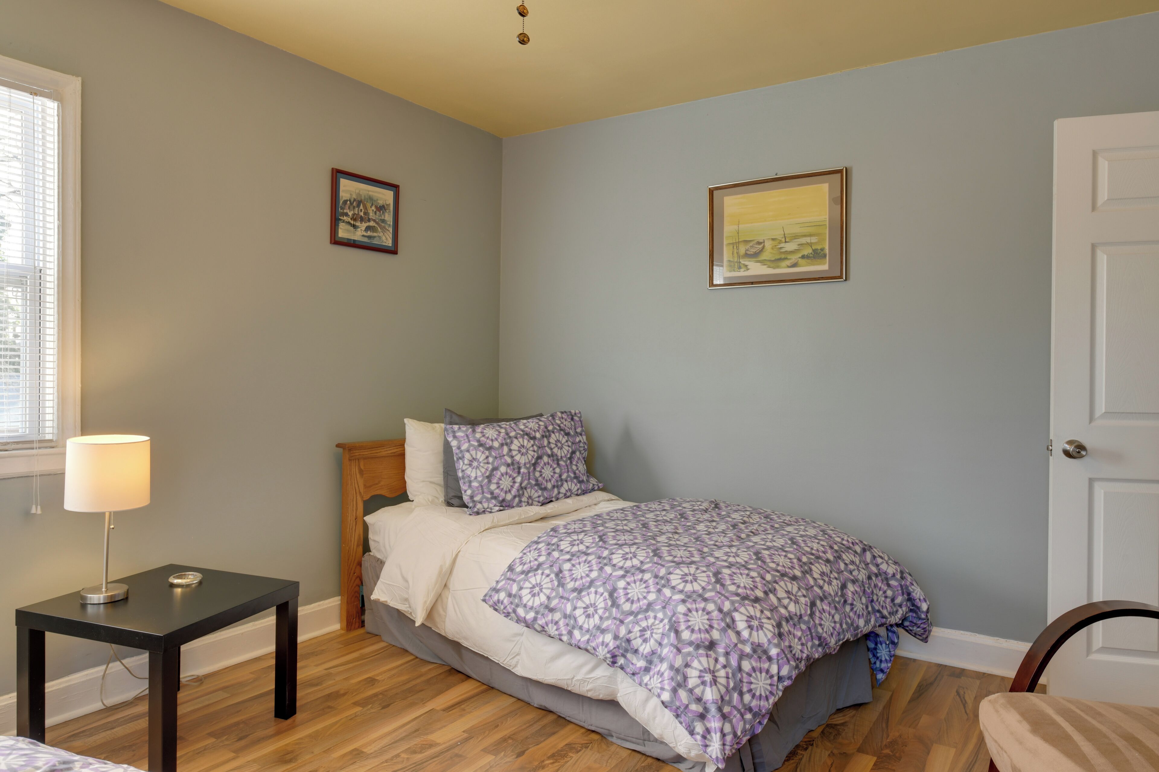A bedroom with a bed, a bedside table with a lamp, and two framed pictures on the wall.