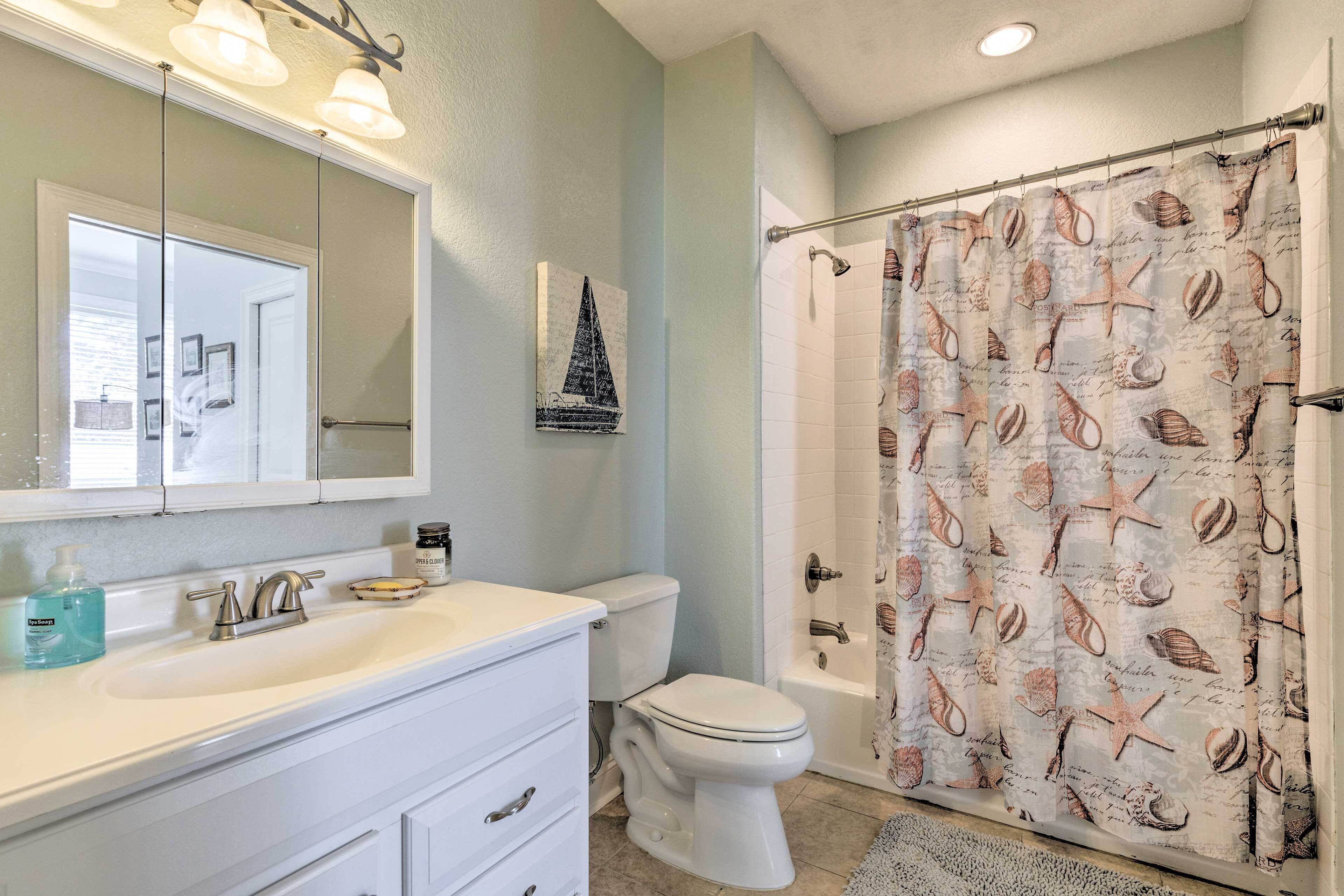 A bathroom with a white sink, a mirror, a toilet, and a shower curtain with a nautical theme.