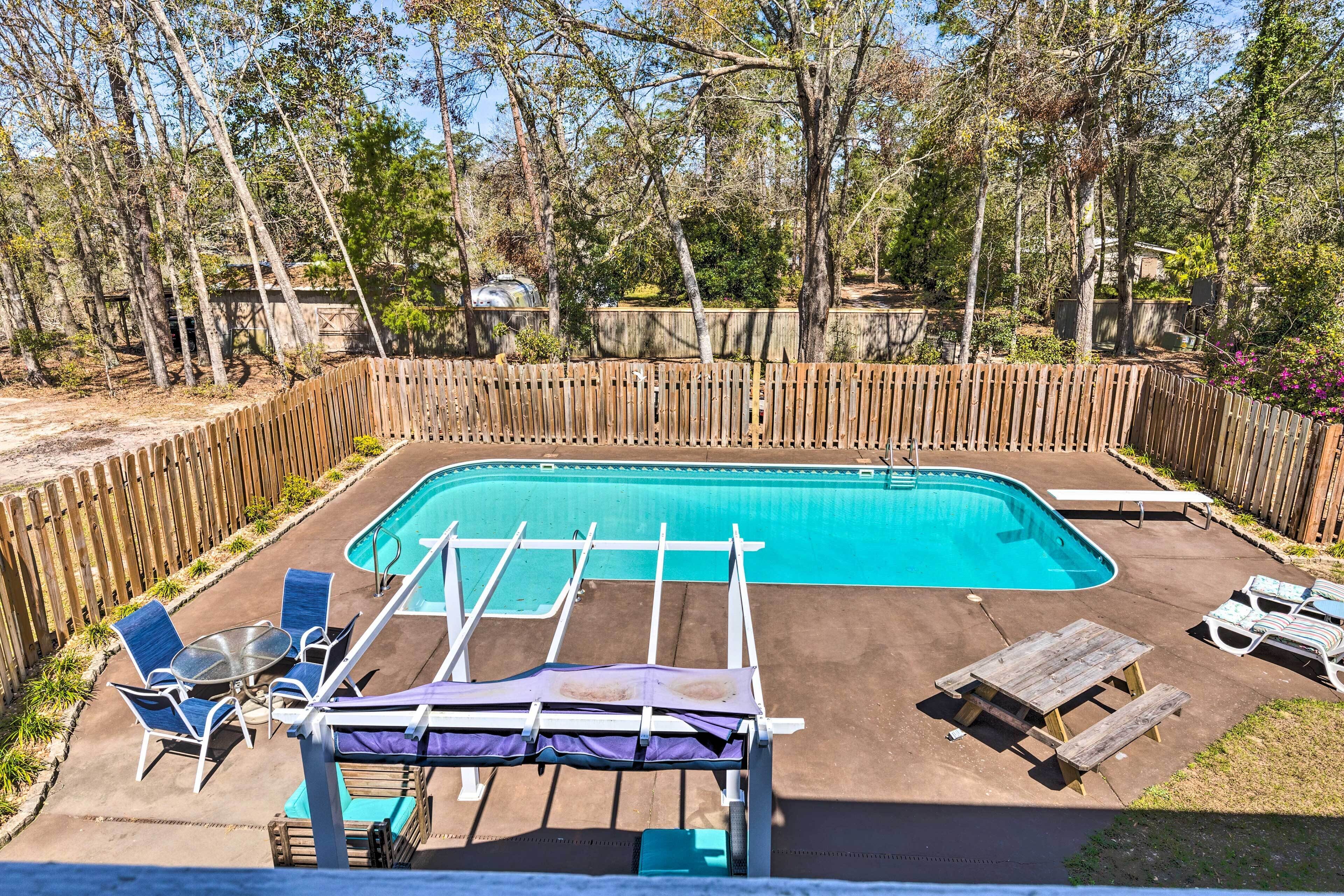 A backyard with a swimming pool, wooden deck, lounge chairs, and a covered picnic table.