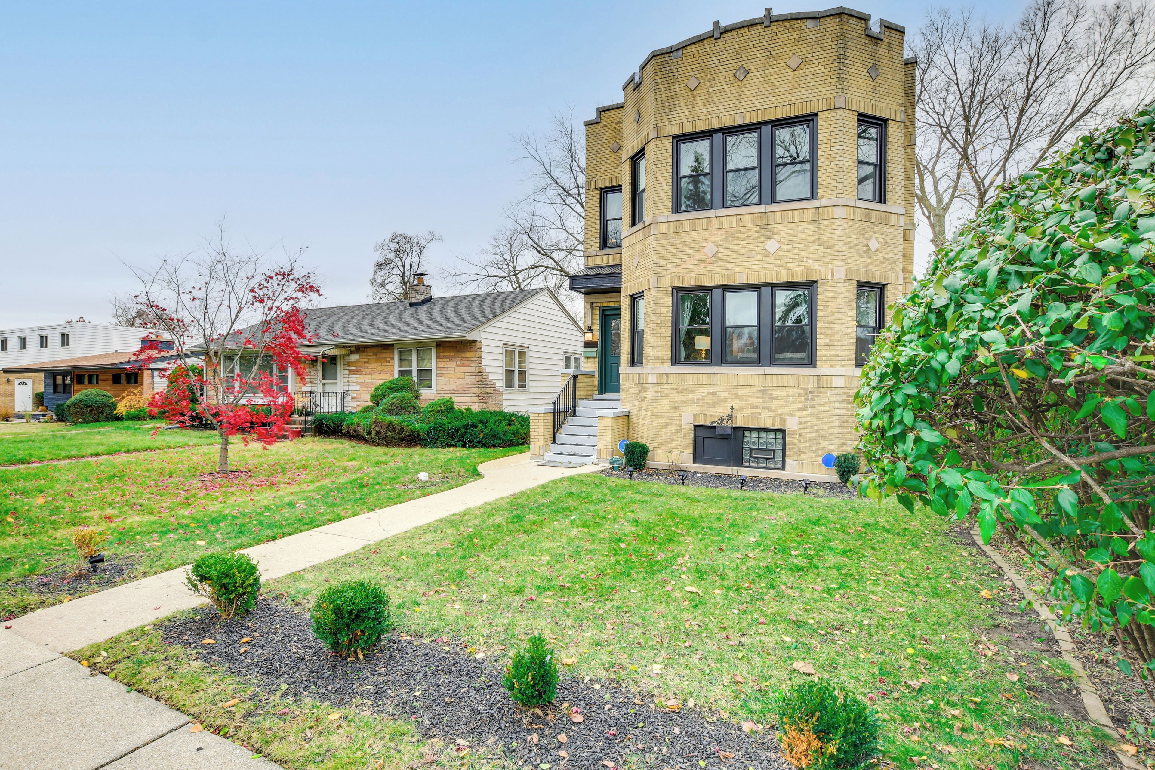 A modern two-story house with a brick facade, a front yard with a pathway, and a small garden area.