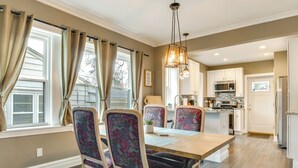 A dining area with a wooden table and patterned chairs, a kitchen in the background, and a window with curtains. - Pet-friendly Family Apartment - Near NU Campus! (Evanston)