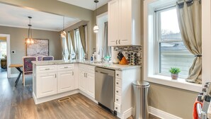 A modern kitchen with white cabinets, a dishwasher, and a window with curtains. - Pet-friendly Family Apartment - Near NU Campus! (Evanston)