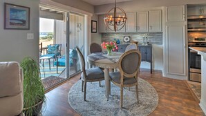 A dining area with a round table, chairs, and a chandelier. There is a view of a balcony with outdoor furniture. - Waterfront Lake Travis Home w/ Pool Access! (Leander)