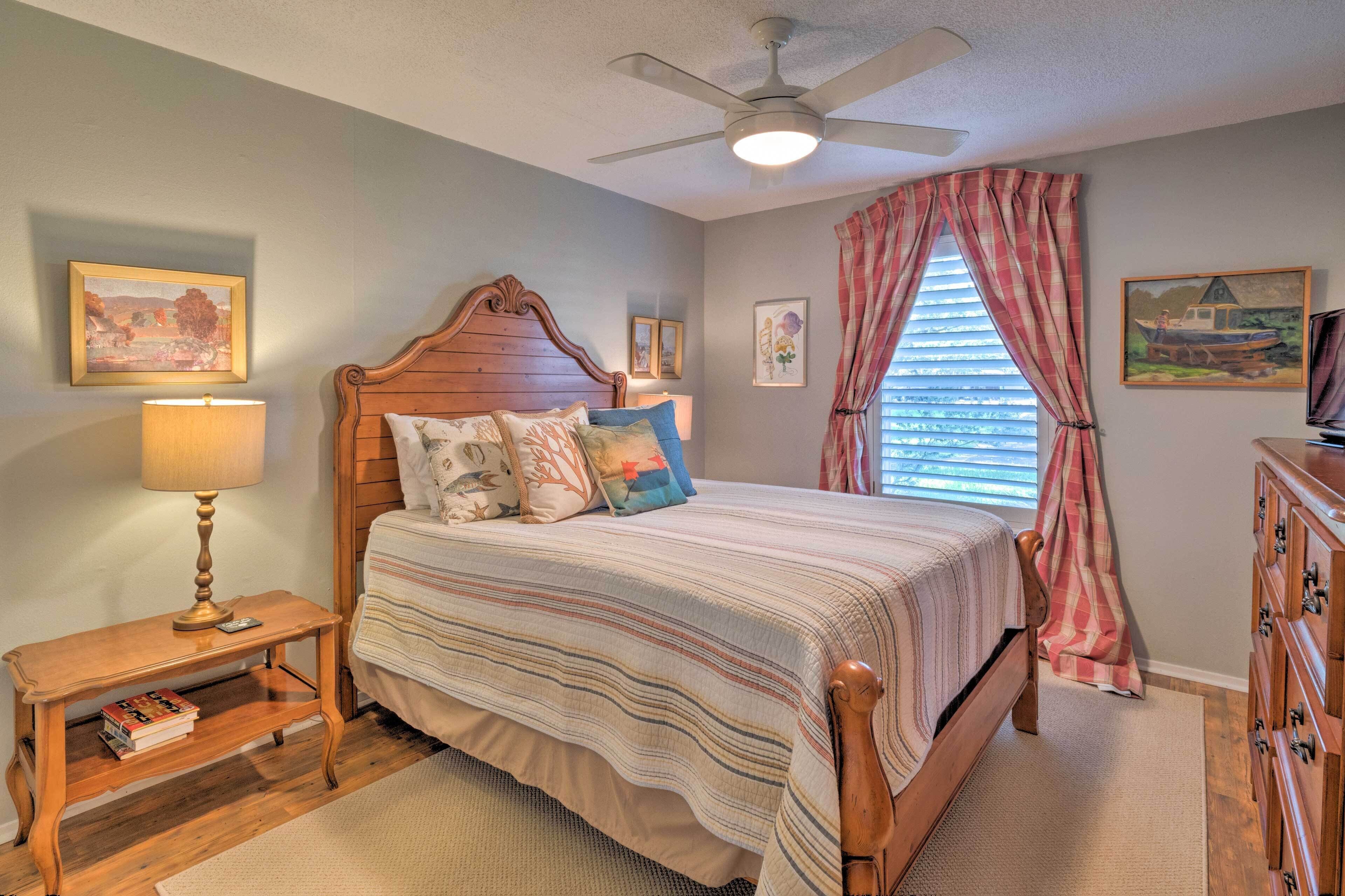 A bedroom with a wooden bed, a nightstand with a lamp, a ceiling fan, and a window with curtains.